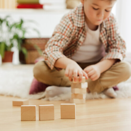 Little child sitting on the floor. Pretty boy palying with wooden cubes at home